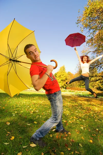 Engraçado casal com guarda-chuvas no fundo do outono (foco em um cara — Fotografia de Stock
