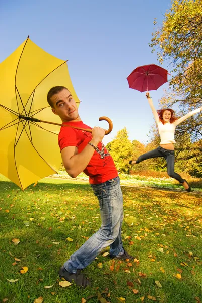 Engraçado casal com guarda-chuvas no fundo do outono (foco em um cara — Fotografia de Stock