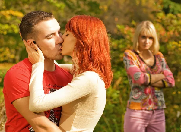 年轻的情侣接吻和冒犯的姑娘站在背景 浅景深 重点放在对夫妇 — 图库照片