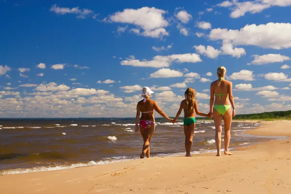 Madre y dos hijas caminando en una playa cerca del agua — Foto de Stock