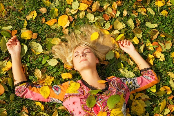 Vacker blond flicka liggande på hösten lämnar — Stockfoto