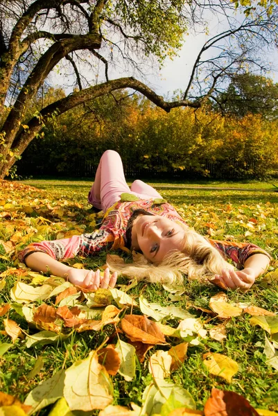 Menina loira bonita deitada em folhas de outono — Fotografia de Stock