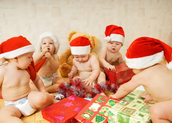 Группа очаровательных малышей в рождественских шляпах упаковывает подарки Лицензионные Стоковые Фото