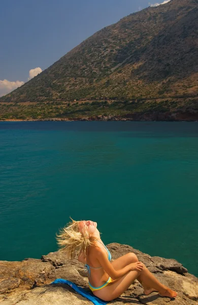 美丽的金发女孩坐在海边岩石上 — 图库照片