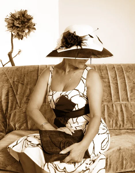 Sépie tónovaný obraz ženy s kloboukem sedí na pohovce — Stock fotografie
