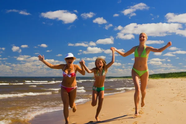 Mãe e duas filhas correndo em uma praia perto da água — Fotografia de Stock