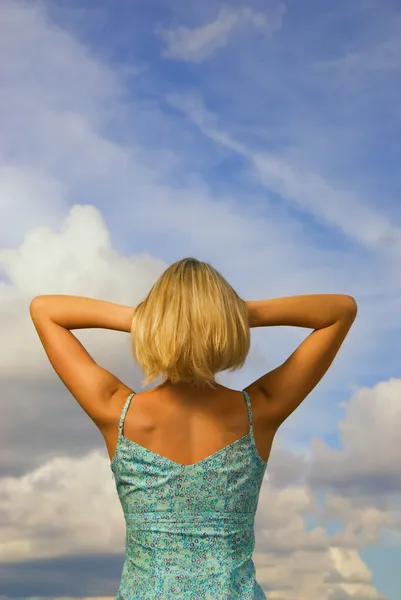 Blond meisje achter blauwe bewolkte hemel als achtergrond — Stockfoto