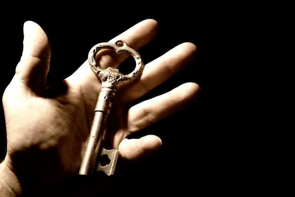 Mano umana con una vecchia chiave isolata su sfondo nero — Foto Stock