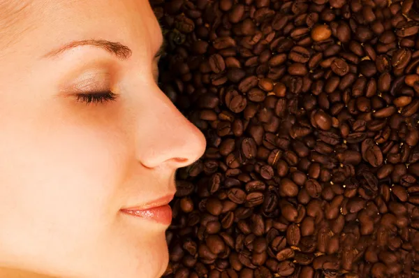 Vackra flickans ansikte på över kaffebönan bakgrund — Stockfoto
