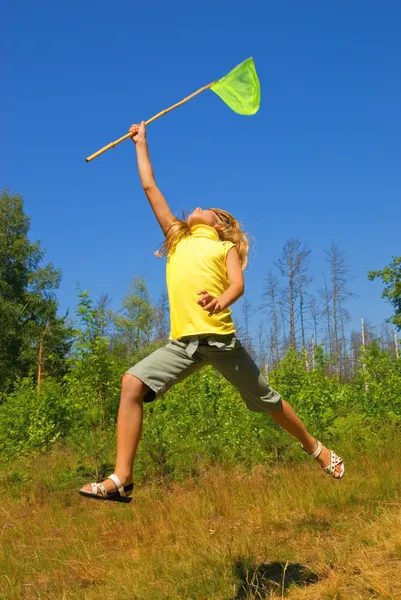 Junges Mädchen mit Schmetterlingsnetz springt auf eine Wiese — Stockfoto