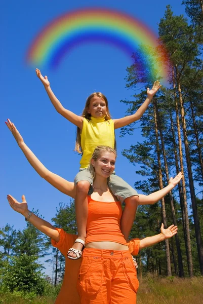 Kleines Mädchen, das auf den Schultern einer Schwester sitzt und den Regenbogen in der Hand hält — Stockfoto