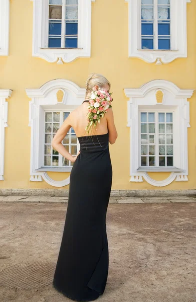 Beautiful blond girl in black evening dress with a boquet — Stock Photo, Image