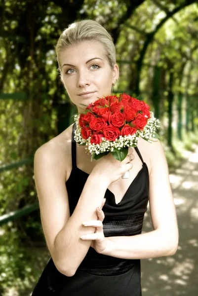 赤い ros の花束を開催のイブニング ドレスの美しいブロンドの女の子 — ストック写真