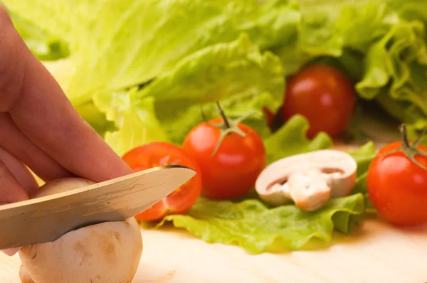 Mão com um cogumelo de corte de faca, alguns vegetais no backg — Fotografia de Stock