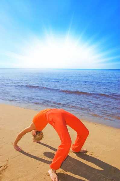 Blond meisje toont dat wat yoga beweegt op het strand — Stockfoto