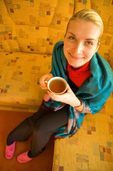 Chica rubia divertida con una taza de café sentado en el sofá — Foto de Stock