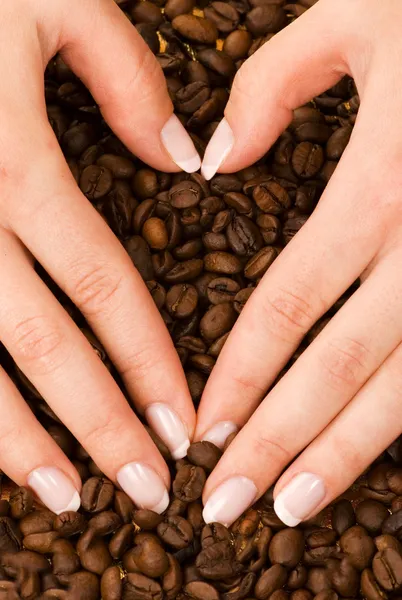 Forma de corazón con las manos por encima de granos de café — Foto de Stock