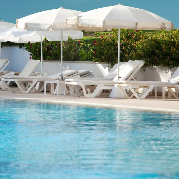 Plankasängar med paraplyer på pool — Stockfoto
