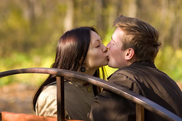 Jovem casal beijo em um banco no parque — Fotografia de Stock