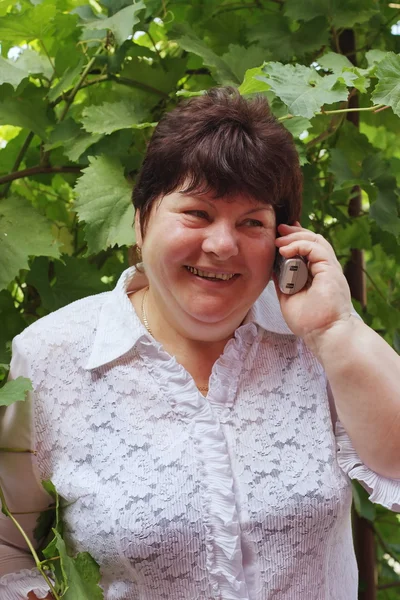 En äldre kvinna på naturen talar via telefon — Stockfoto