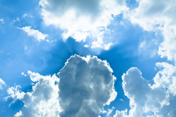 Zon achter witte pluizige wolken in de blauwe hemel — Stockfoto