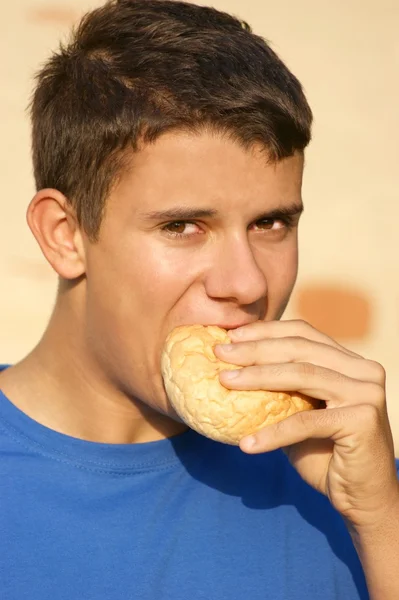 Un adolescent mâle mangeant un pain roulé — Photo