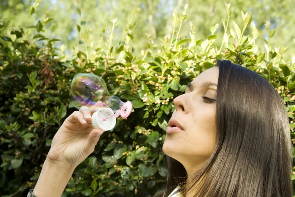 Молодая женщина пускает пузыри в зеленом парке — стоковое фото