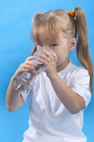 stock image Small cute girl is drinking water on blue background