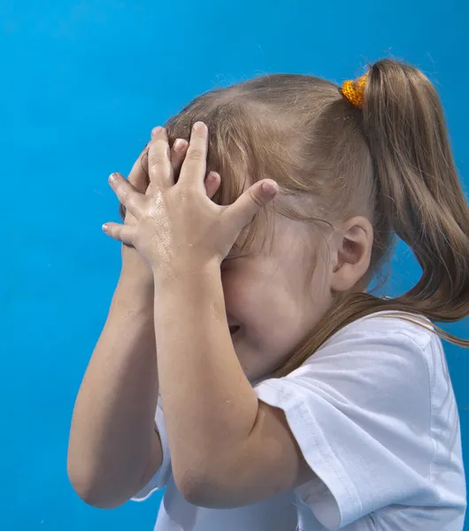 Маленька дівчинка прикриває обличчя руками ізольовано на синьому — стокове фото