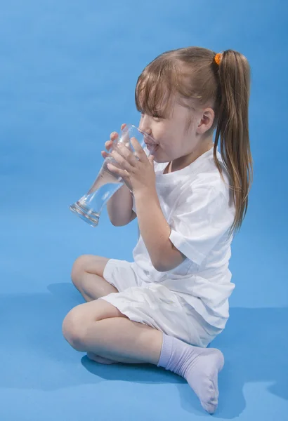 Menina bonito pequeno é beber água no fundo azul — Fotografia de Stock