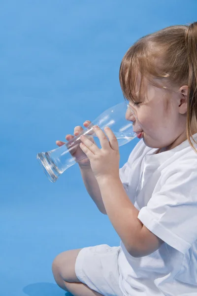 Menina bonito pequeno é beber água no fundo azul — Fotografia de Stock