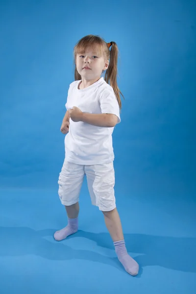 Kleine ernstige meisje is die zich voordeed als vechter geïsoleerd op blauw — Stockfoto