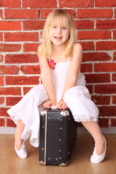 Красивая маленькая девочка сидит на чемодане — стоковое фото