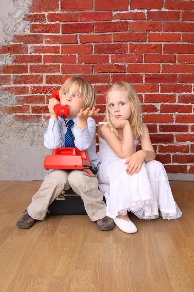 Piękne dzieci siedzą na torbie. Emocjonalna rozmowa telefoniczna. — Zdjęcie stockowe