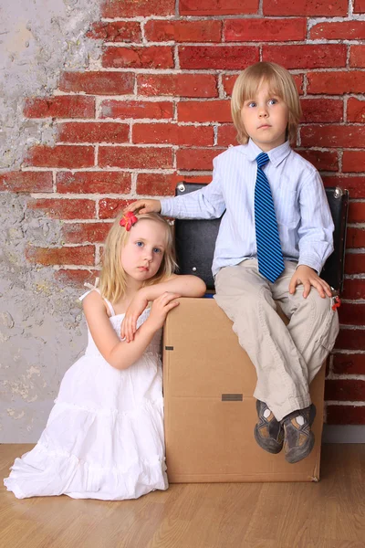 Niño y niña sentados en una caja de cartón y una maleta. Muévete. —  Fotos de Stock
