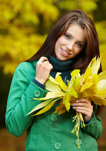 Fashion woman in autumn park holding yellow leaf — Stock Photo, Image