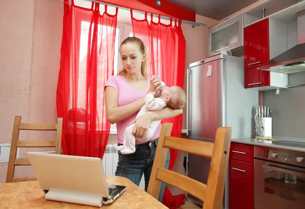 La madre joven en la cocina con el portátil —  Fotos de Stock
