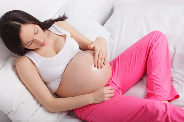 Mulher grávida pondo uma nata em um estômago — Fotografia de Stock
