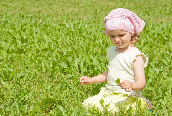 A little girl sits on a green lawn — Stock Photo, Image