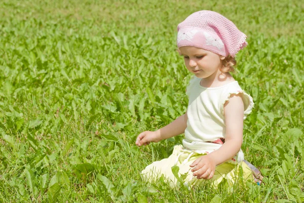 A little girl sits on a green lawn — Stock Photo, Image