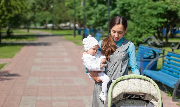My mother carries a child in her arms and rolls the stroller in — Stock Photo, Image