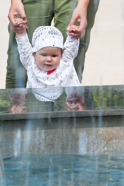 Een klein meisje kijkt omhoog naar de fontein, houden van zijn moeder arm — Stockfoto