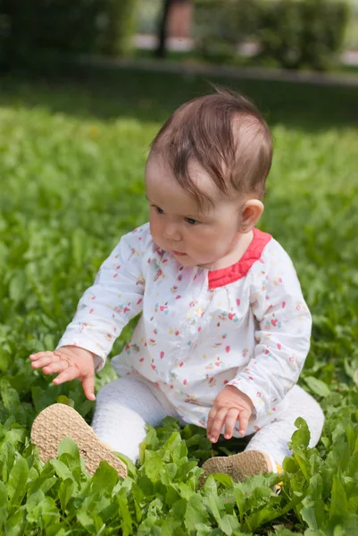 En liten flicka sitter på grönt gräs i parken — Stockfoto