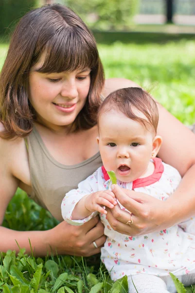 Glückliche Mutter mit einem kleinen Mädchen, das auf dem Rasen im Park ruht — Stockfoto