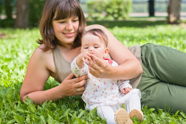Mamá feliz con una niña descansando sobre la hierba en el parque —  Fotos de Stock