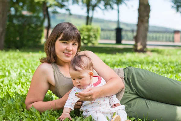 Mamá feliz con una niña descansando sobre la hierba en el parque —  Fotos de Stock
