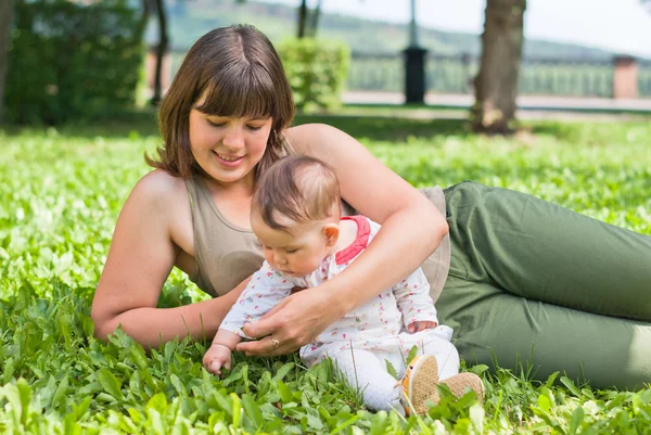 Glad mamma med en liten flicka som vilar på gräset i parken — Stockfoto
