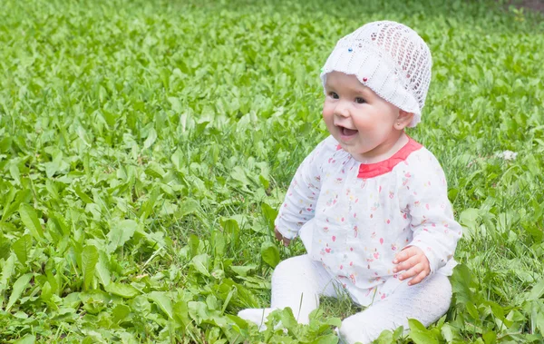 Een klein meisje, zittend op groen gras in het park — Stockfoto