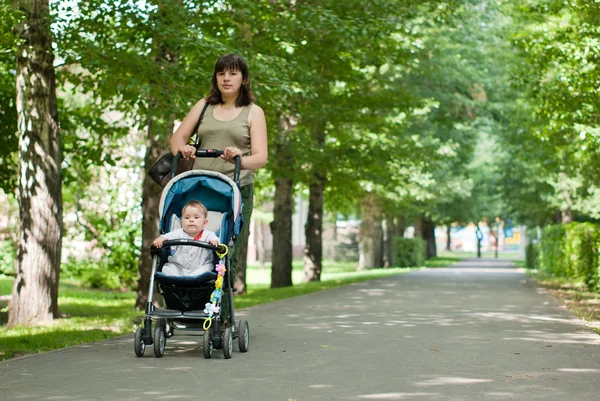 A young mother walking with a baby carriage in the park — Stock Photo, Image