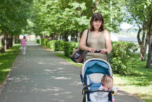 Μια νεαρή μητέρα, περπάτημα με ένα baby μεταφορά στο πάρκο — Φωτογραφία Αρχείου
